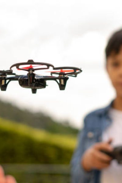 Concentrated boy flying his toy drone with remote control in his hands in a park. Selective focus