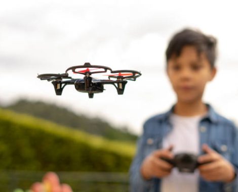 Concentrated boy flying his toy drone with remote control in his hands in a park. Selective focus